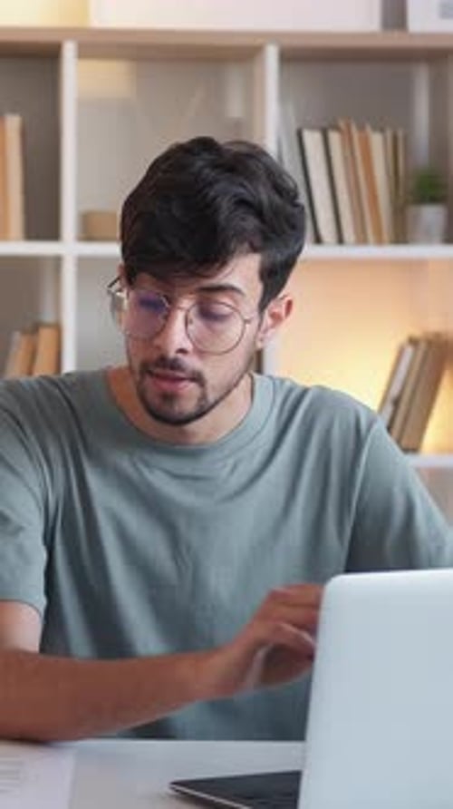 Young Man Thinking at Desk with Laptop