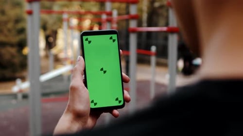 Sportsman Looking at the Smartphone with a Mockup Green Screen Standing in the Outdoor Workout Area