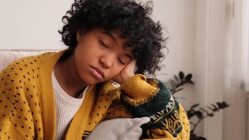 Jeune fille afro-américaine triste, pensive et démotivée assise sur un canapé à la maison à l'intérieur