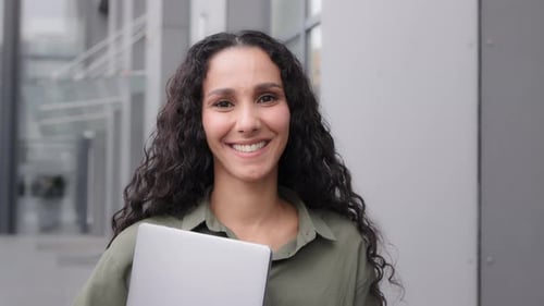 Smiling Woman Holding Laptop Outside Modern Building