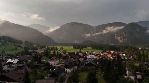 Aerial drone view of a small alpine village nestled among green mountains and forests