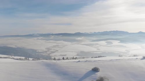 Left flying aerial over snowed-in hill with mountain range in backdrop