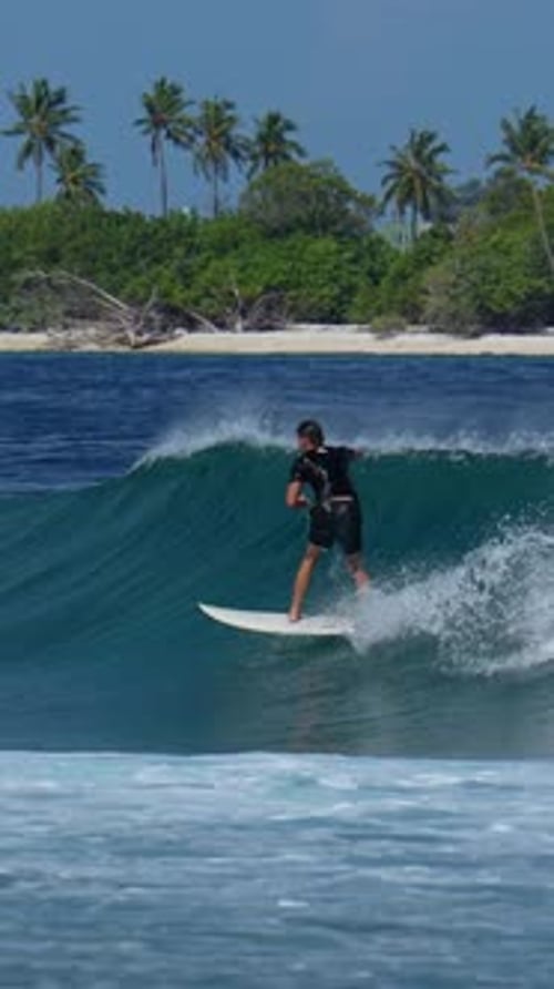 Surfer Rides Turquoise Wave Towards Tropical Island Paradise