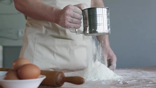Ein Koch in einer Bäckereiküche sieben Mehl durch ein Sieb und beginnt mit der Zubereitung von Brot.