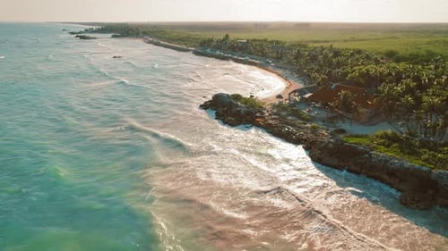 Vista aérea do litoral com palmeiras na praia e ondas turquesas ao pôr do sol