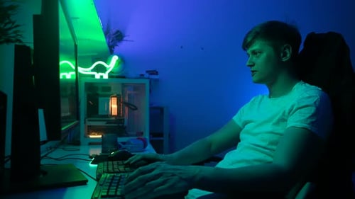 Side View of Male Gamer Sitting at Computer Desktop Monitor and Playing Virtual Online Video Game