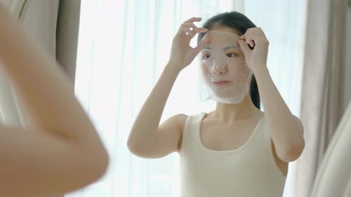 Woman Applying Facial Mask in Front of Mirror
