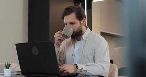 Man Drinking Coffee While Working on Laptop at Home