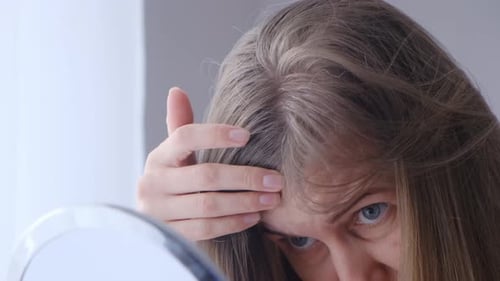 Adult Woman Examines Hair Roots in Mirror