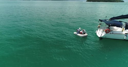 Aerial drone orbiting close up shot of two guys getting of a sail boat and starting the motor on a s