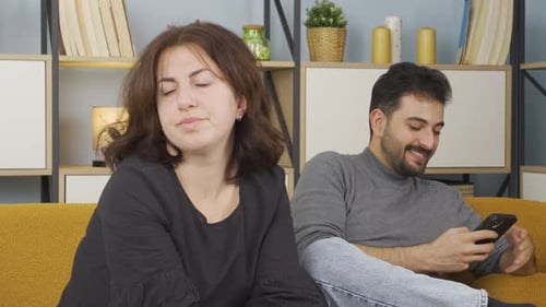 Woman Upset While Man Uses Smartphone on Couch