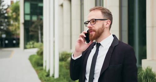 Businessman talk mobile phone in city near business office building. Man talking smartphone outdoors