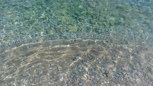 Crystal clear ocean water as seen from beach with stones and sand