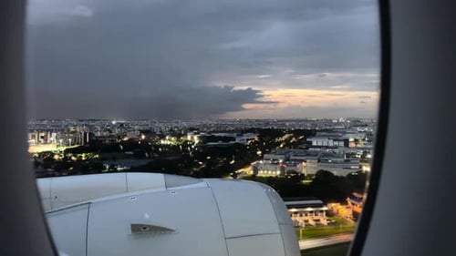 Aerial View Through Airplane Window Of City Buildings In Singapore At Sunset With Thunder Lightning