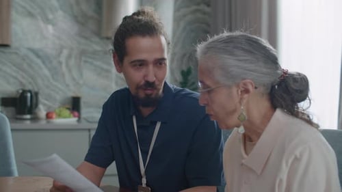 Social Worker Explaining Financial Document to Senior Woman during Home Visit