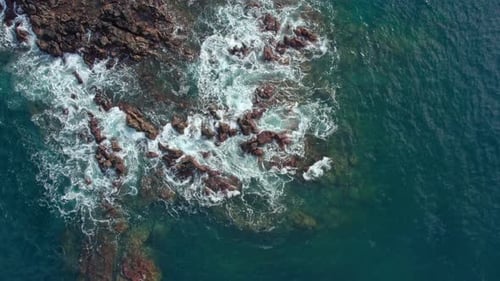 Slow Motion Drone Orbit of Turquoise Ocean Waves Crashing on Coastal Rocks
