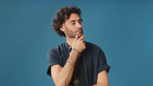 Pensive man rubbing his chin and looking side isolated on blue background in studio