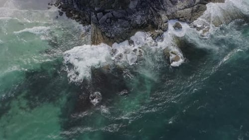Waves breaking along a rocky shoreline, aerial fly over