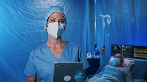 Frustrated Doctor With Tablet By Patient Laying On Bed In Hospital, Coronavirus Concept.