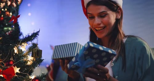 Young Woman Opening Christmas Gift Near Tree