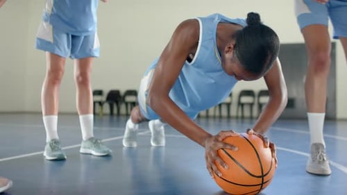 Exercising in gym, female basketball player doing push-ups using basketball