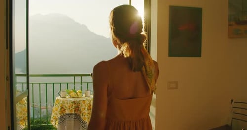 A woman captures the sunrise from a balcony. Illuminated by morning light, the scene reveals a seren