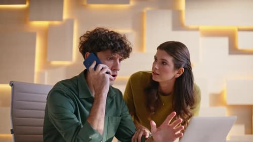 Man on phone with worried colleague looking at laptop