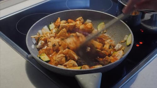 Cooking chicken and vegetables in a frying pan, stirring with a wooden spoon. CLOSE UP.
