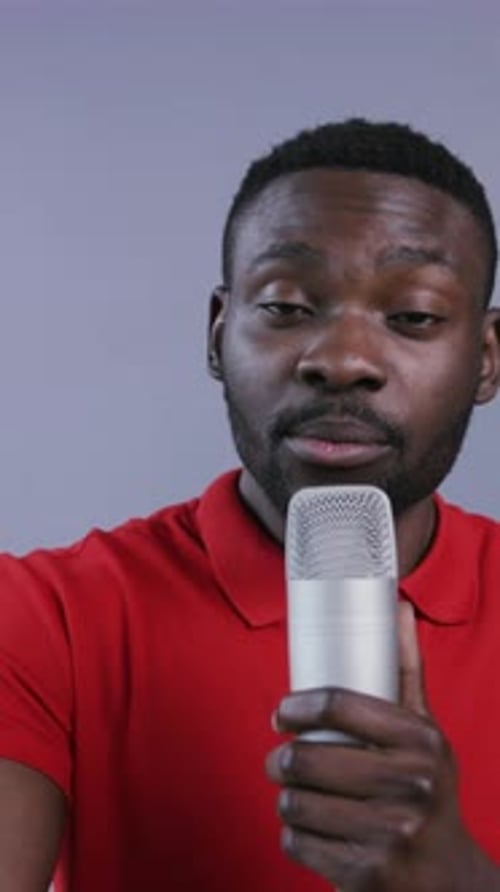 Man Speaking Into a Microphone on Grey Background