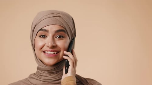 Young Muslim Woman Smiling While Talking on the Phone in a Studio Setting