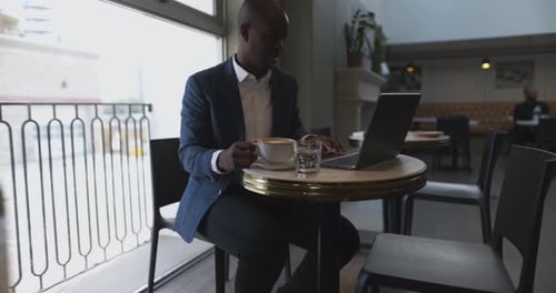 Mature businessman enjoys cappuccino reading email at laptop in cafe