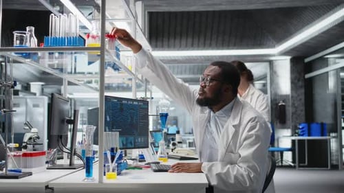Clinical Microbiologist in Lab Looking at Blood Sample in Test Tube Using PC