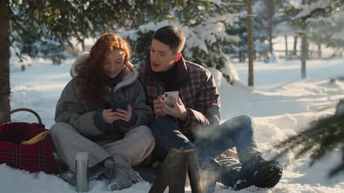 A Man with His Wife with Phones During a Halt in the Winter Forest A Young Couple Sitting on a Halt