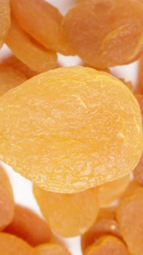 Vertical video. Top view, dried apricot rotates against the background of a heap of other apricots.