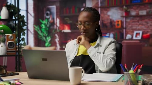Woman in Home Office Stretches Back Feeling Fatigued While Working on Laptop