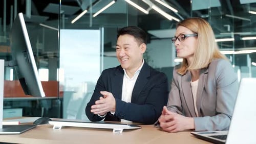happy smiling cheerful coworkers discuss project strategy by looking and pointing at laptop pc