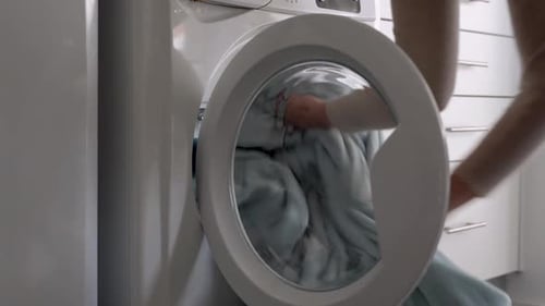 Female put blanket into laundry machine, Load clothes to washer machine and close door.