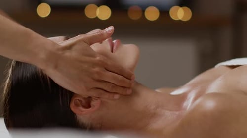 Young Tranquil Woman Getting Relaxing Face Lifting Massage at Spa Salon Resting on Massage Bed Side
