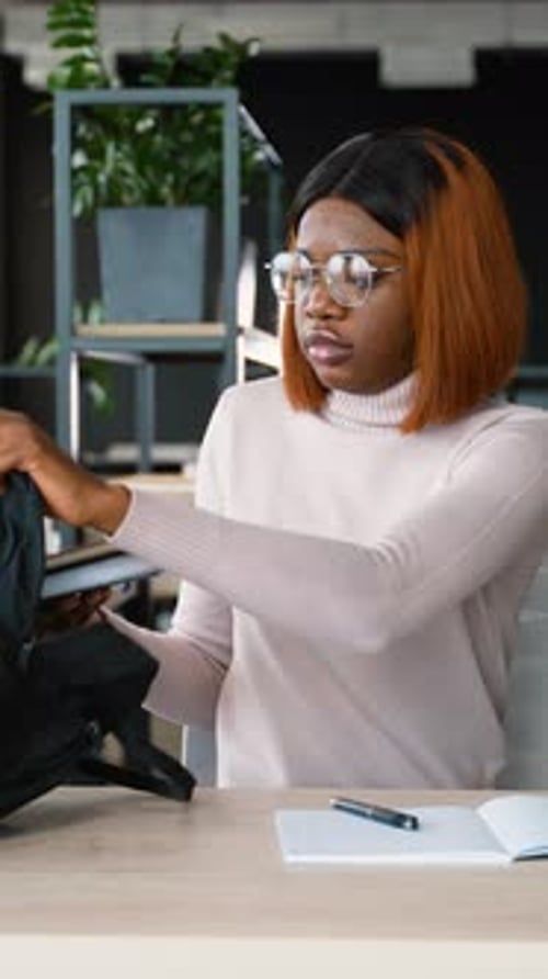 Woman Puts Tablet into Backpack at Desk