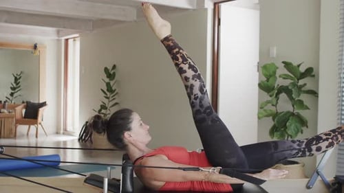 Fit senior caucasian woman stretching on reformer in pilates studio, unaltered, in slow motion