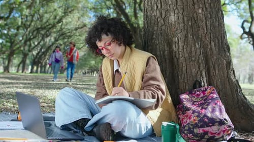Junge Studentin benutzt Laptop und macht sich Notizen im Park