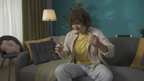 Young Man with Heartburn on Couch Drinks Water