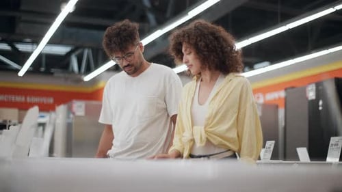 Young couple choosing washing machine in electronics store in slow motion