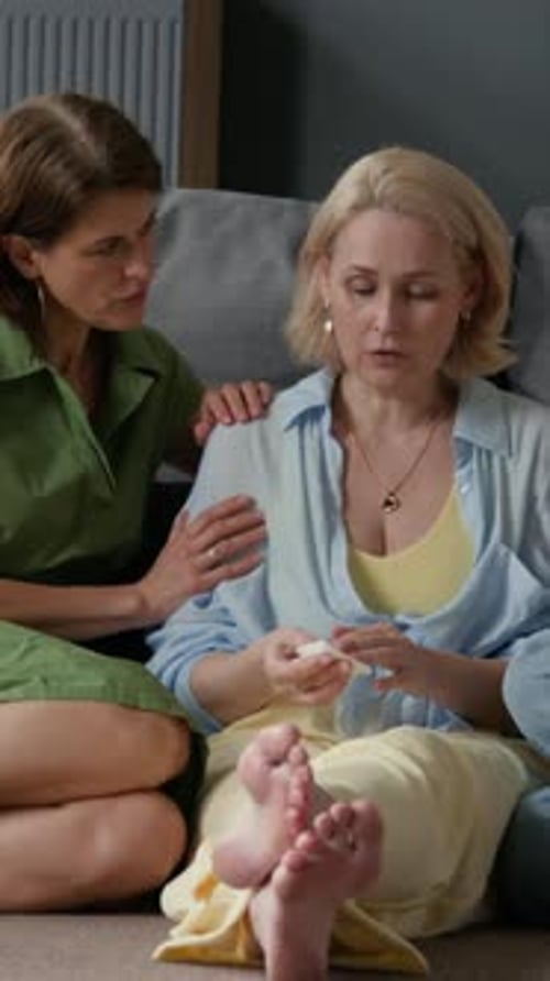 Mujeres maduras consolando a su angustiada amiga, llorando en un pañuelo de papel en el suelo