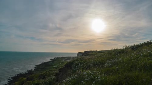 Eine ruhige Küstenlandschaft unter einem weiten Himmel, in der die Sonne sanft über das Meer und die Klippen strahlt