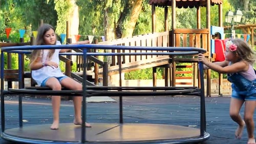 Zwei kleine Mädchen auf dem Spielplatz, die sich an einem heißen Sommertag auf einem Karussell amüsieren
