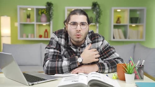 Young Adult Studying with Laptop and Book at Home