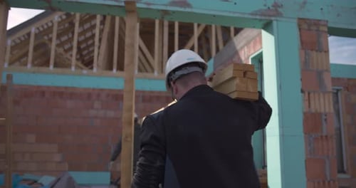 Workers carrying wooden planks at construction site, collaboration in building residential