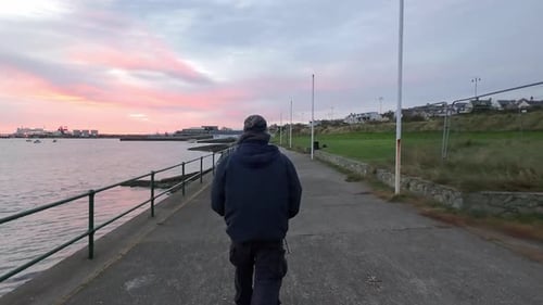 Homme marchant seul sur le front de mer du port sous un lever de soleil brillant tôt le matin en contemplation