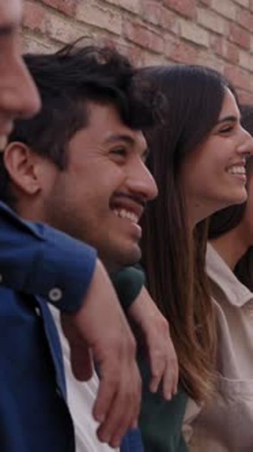 Lateral View Group of Cheerful Friends Together Leaning on Brick Wall Laughing Hugging Outdoors